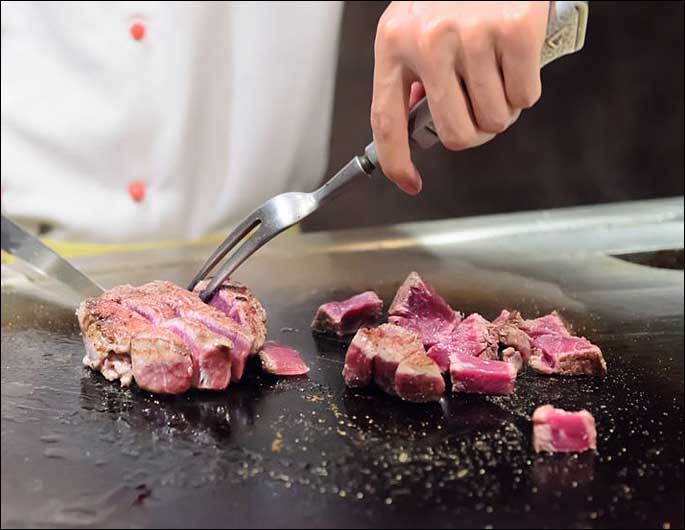 chef cooking meat on commercial gas griddle in restaurant kitchen