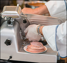 image of restaurant or deli employee using commercial food slicer